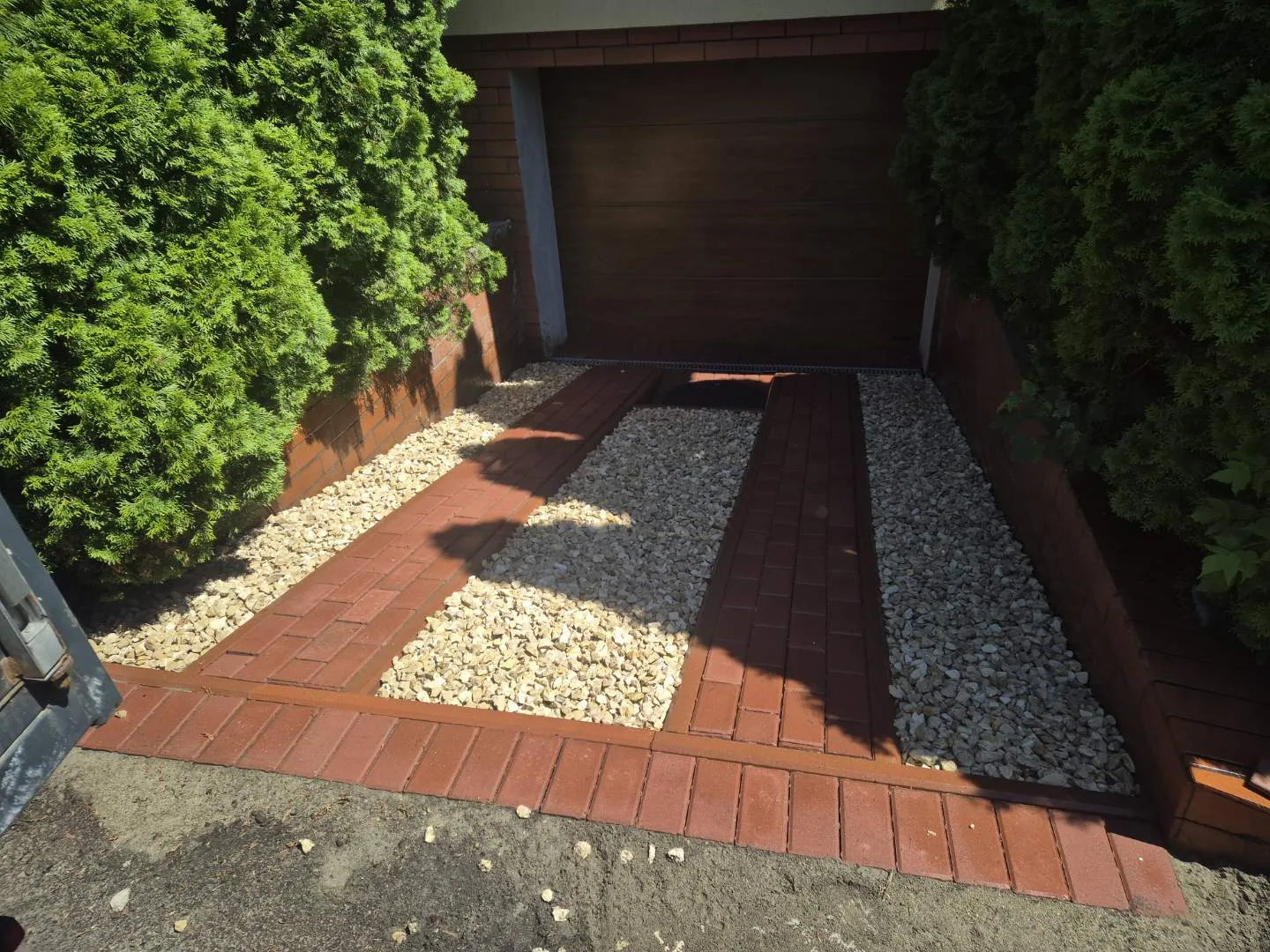 Wykonany dojazd do garażu z nowoczesnym układem z czerwonej kostki brukowej i białego kruszywa