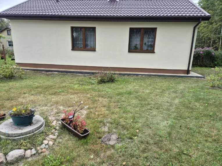 Zdjęcie przedstawia nowy dom z tynkowaną elewacją i dachem, będący efektem końcowym prac budowlanych