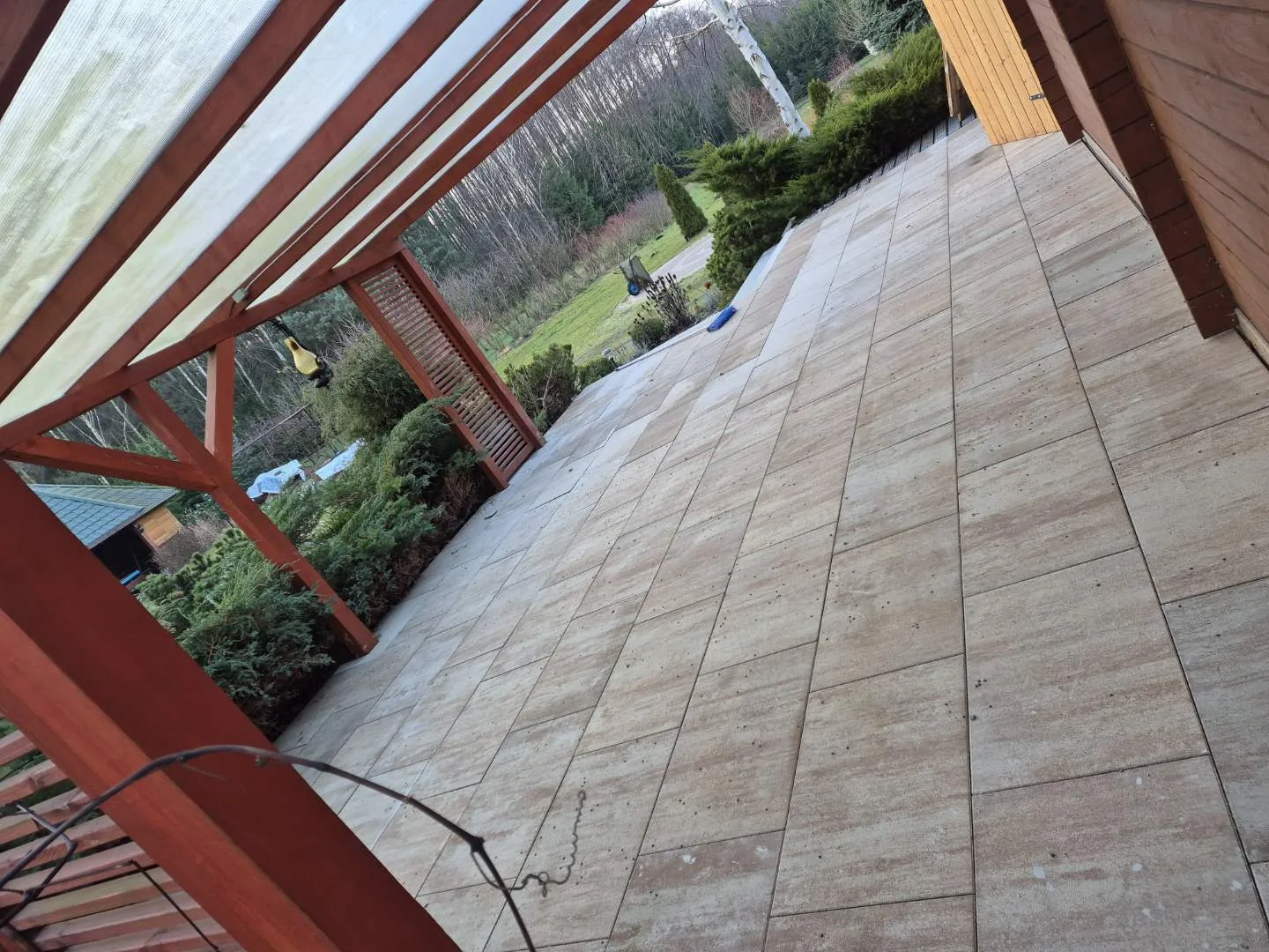 Budowa nowoczesnego tarasu z wykorzystaniem dużych płyt kamiennych w zadaszonej konstrukcji drewnianej