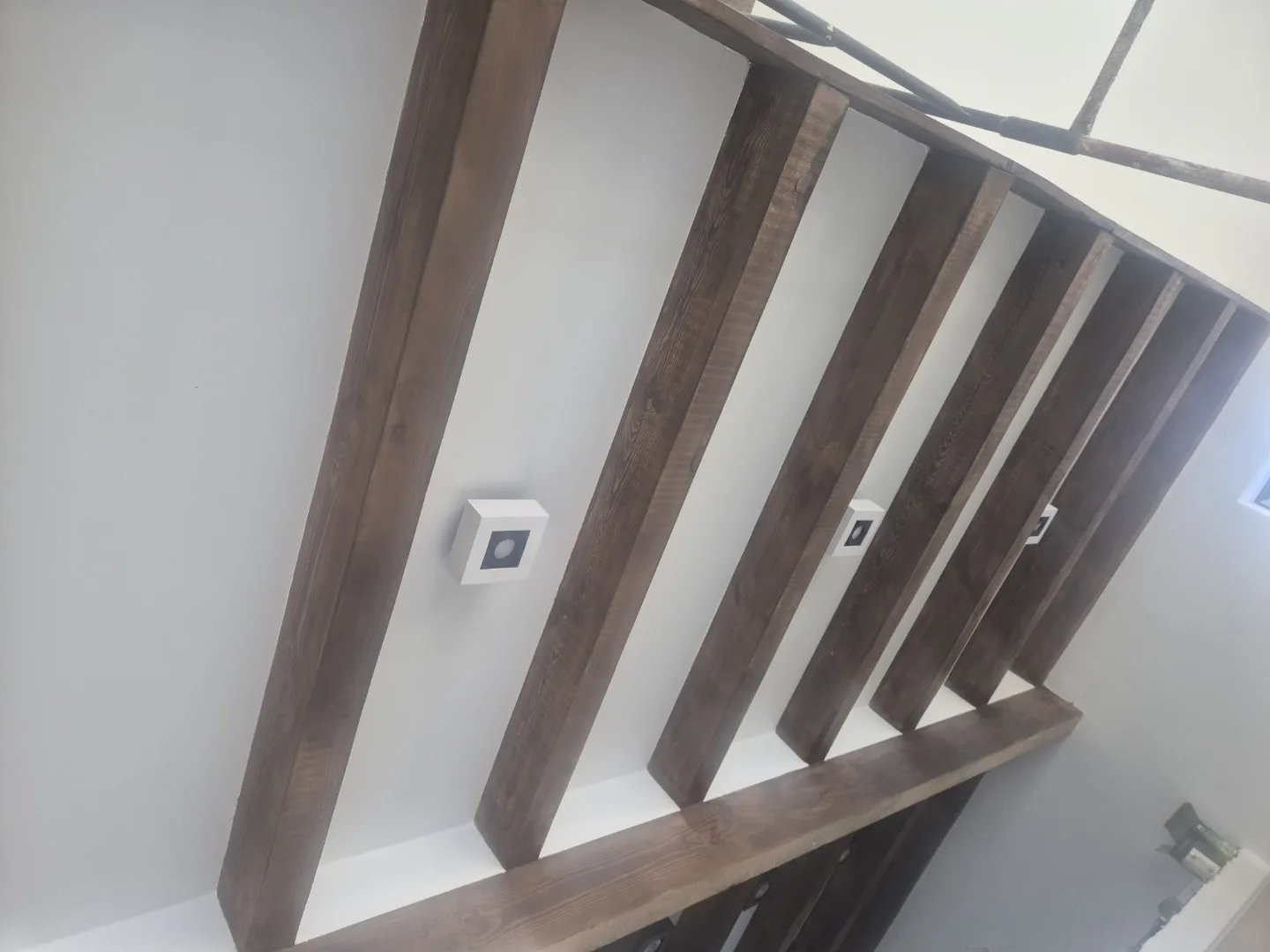 Zdjęcie przedstawia ciemne drewniane belki schodowe zamontowane na białej ścianie